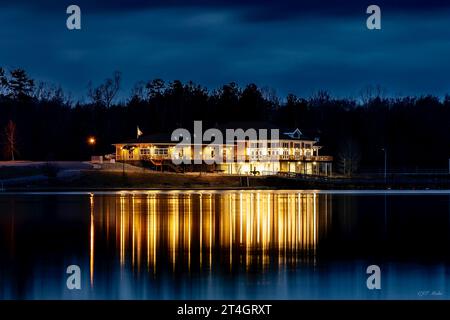 Ein modernes Hochhaus, beleuchtet bei Nacht, am Ufer eines ruhigen Sees gelegen Stockfoto