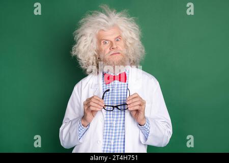 Foto eines ernsten funky lustigen verrückten verrückten Arztes mit unordentlichen Haaren halten Brille isoliert auf grünem Farbhintergrund Stockfoto