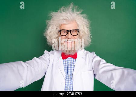 Foto des verrückten Genies reifer Erfinder gekleidet weiße Uniform-Fliege Brille, die Selfie-lokalisierter grüner Hintergrund schwenken Stockfoto