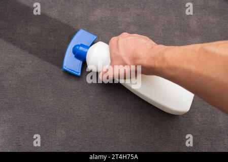 Der Mann putzt das Sofa. Auftragen eines chemischen Fleckenentferners auf die Oberfläche. Entfernen von Flecken von einem Sofa. Reinigung des Hauses. Stockfoto