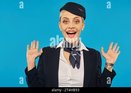 Porträt der staunenden und freudigen Stewardess in Uniform mit Wow-Geste auf blauem Hintergrund Stockfoto