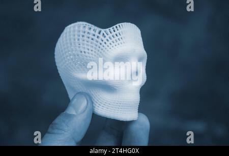 Person mit Fingern der Hand kleiner Prototyp eines menschlichen Schädels in 3D gedruckt aus geschmolzenem weißem Kunststoff. Dreidimensionales Modell. Additive progressive Medizintechnik. Moderne neue Druckindustrie. Stockfoto
