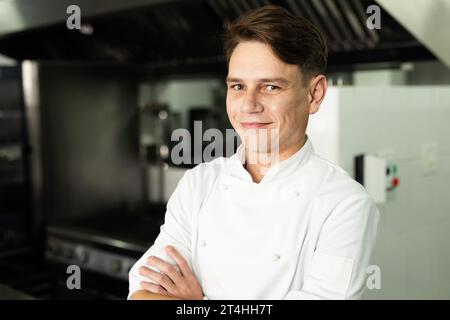 Porträt eines lächelnden weißen Küchenchefs mit überkreuzten Armen, der selbstbewusst in der Küche steht Stockfoto