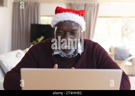 Glücklicher afroamerikanischer Seniorenmann mit weihnachtsmütze, der zu Hause Laptop-Videoanrufe macht Stockfoto