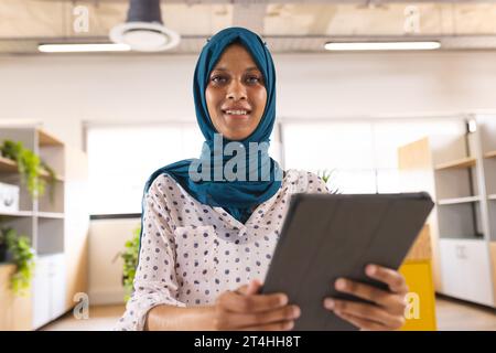 Porträt einer glücklichen birassischen Geschäftsfrau mit Hijab, die Videoanrufe im kreativen Büro macht Stockfoto