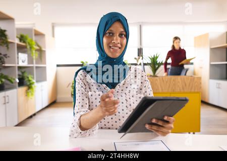 Porträt einer glücklichen birassischen Geschäftsfrau mit Hijab, die Videoanrufe im kreativen Büro macht Stockfoto