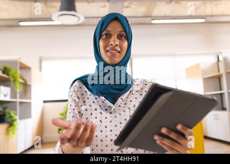 Porträt einer glücklichen birassischen Geschäftsfrau mit Hijab, die Videoanrufe im kreativen Büro macht Stockfoto