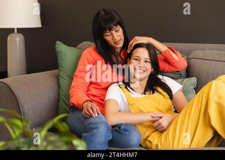 Glückliche, vielfältige Mutter und Tochter, die auf der Couch sitzen und zu Hause umarmen, Kopierraum Stockfoto