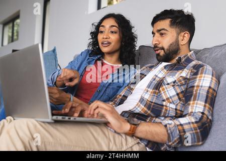 Glückliches birassisches Paar, das auf dem Sofa sitzt und im Wohnzimmer zu Hause einen Laptop benutzt Stockfoto