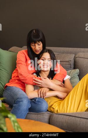 Glückliche, vielfältige Mutter und Tochter, die auf der Couch sitzen und zu Hause umarmen, Kopierraum Stockfoto