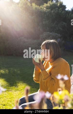 Glückliche ältere Frau, die Tee trinkt, sitzt im Garten Stockfoto