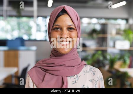 Porträt einer glücklichen birassischen Geschäftsfrau mit Hijab im kreativen Büro Stockfoto