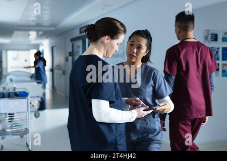 Verschiedene Ärztinnen diskutieren Arbeit, mit Tablette im Flur im Krankenhaus Stockfoto