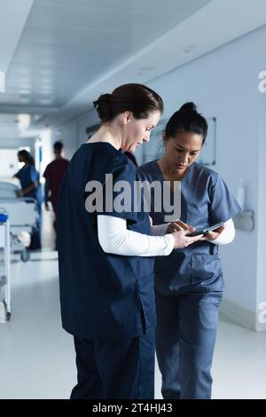 Verschiedene Ärztinnen diskutieren Arbeit, mit Tablette im Flur im Krankenhaus Stockfoto