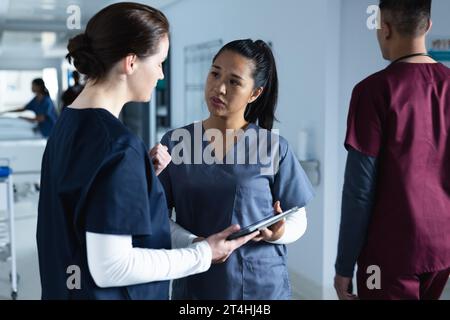 Verschiedene Ärztinnen diskutieren Arbeit, mit Tablette im Flur im Krankenhaus Stockfoto