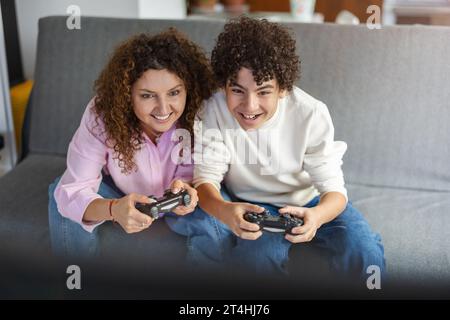 Mutter und Sohn spielen Videospiele, während sie zu Hause auf dem Sofa sitzen Stockfoto