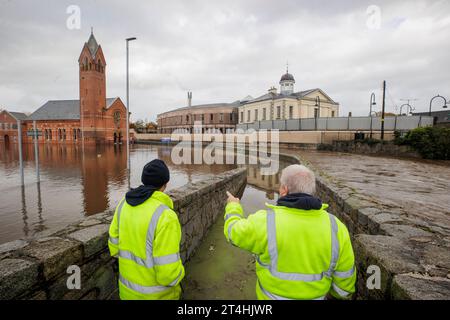 DFI-Arbeiter betrachten das überflutete Wasser auf einem Parkplatz neben der Riverside Reformed Presbyterian Church (links) und dem Newry Courthouse (rechts) in Newry Town, Co Down. In Teilen Nordirlands wurde von Überschwemmungen berichtet, wobei die Polizei die Menschen aufgrund einer gelben Regenwarnung vor Reisen warnte. Die Met Office Warning für Nordirland ist die zweithöchste Ebene und deckt die Countys Antrim, Down und Armagh ab. Bilddatum: Dienstag, 31. Oktober 2023. Stockfoto