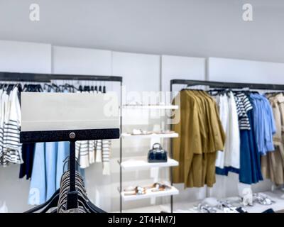 Shopping, leeres oder leeres Preisetikett über verschwommener Kleidung und Kleidung, die in einem legeren Stoffladen gehängt werden. Preisetikett oder Etikett für Freizeitkleidung im Geschäft. Stockfoto