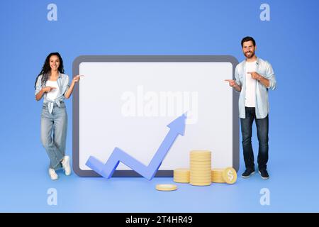 Lächelnde Erwachsene zeigen mit den verschiedenen Familienfingern auf ein großes Tablet mit leerem Bildschirm mit abstrakter Grafik und Münzen Stockfoto