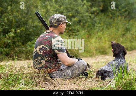 hunter und sein Hund ruhen während der Herbstjagd auf dem gemähten Gras aus Stockfoto
