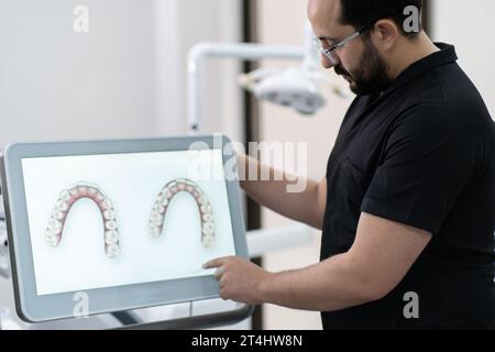 Erfahrener Zahnarzt, der unter- und Oberkiefer-Modelle auf einem Monitor zeigt, der die Zahnbehandlung vorstellt Stockfoto