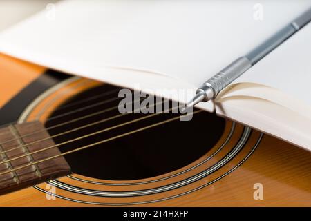 Ein brauner Bleistift und ein dunkelrotes Notizbuch befinden sich auf einer Akustikgitarre. Stockfoto