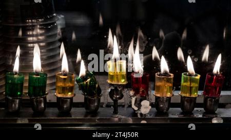 Mehrfarbige Glasfläschchen enthalten Öl und brennende Dochte in einer Menora, die in der achten Nacht des jüdischen Festivals von Hanukka hell leuchtet. Stockfoto