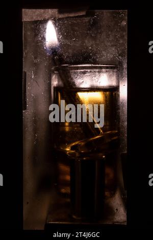 Die Schamasch, oder zusätzliche Helferkerze auf der Menora, leuchtet hell in diesem künstlerischen Bild von Öl-Hanukka-Kerzen, die in einem Glasgehäuse Dura brennen Stockfoto