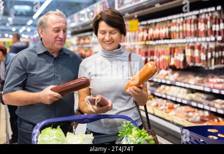 Ältere Gäste, die Würstchen in der Fleischabteilung des Supermarkts suchen Stockfoto