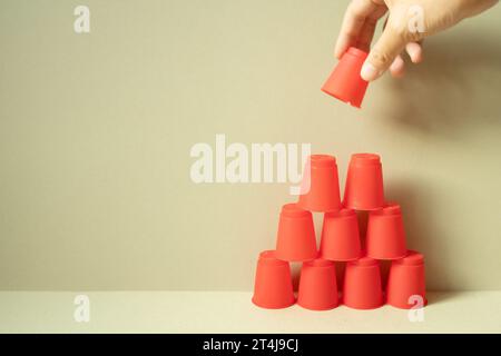 Pyramide aus roten Plastikbechern auf dem Schreibtisch. Khakifarbener beigefarbener Hintergrund. Teamwork Balance Geschäft entwickeln Sie ein Konzept für das Wachstum von Leistungen Stockfoto