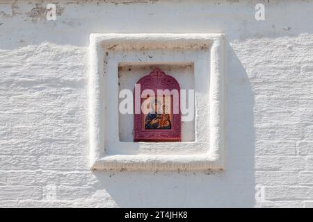 Weiße Backsteinmauer einer orthodoxen Kirche mit einer Keramikfigur der Jungfrau. Stockfoto