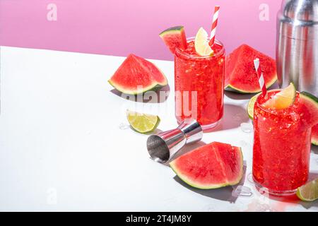 Cocktail aus Wassermelonen-Limonade mit Limette und in Scheiben geschnittener Wassermelone auf einem trendigen, hochfarbigen, weiß-rosa Hintergrund Stockfoto