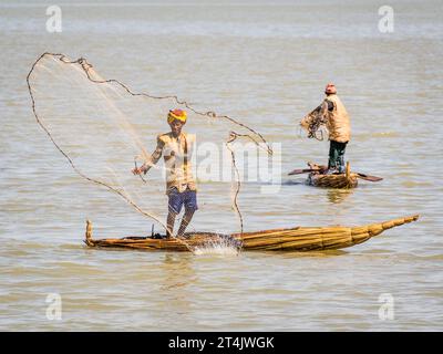 Ein Fischer, der in einem traditionellen Boot steht und ein Fischernetz auswirft Stockfoto