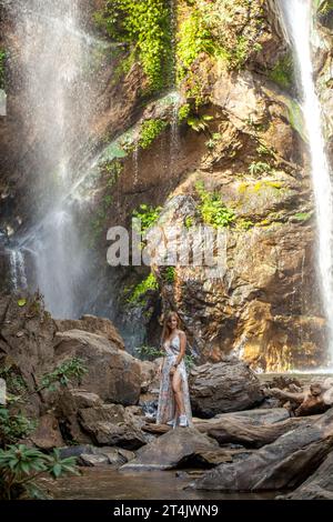 Junge Frau auf Felsen unter dem massiven Wasserfall in Thailand. Stockfoto