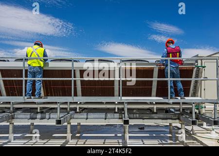 Zwei Bauarbeiter arbeiten an einem adiabatischen Kondensator auf dem Dach eines CO2-Kühllagers (Industriekühlung) Stockfoto