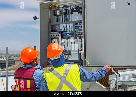 Zwei Bauarbeiter überprüfen die Schalttafel eines adiabatischen Kondensators auf dem Dach eines CO2-Kühllagers (Industriekühlung) Stockfoto