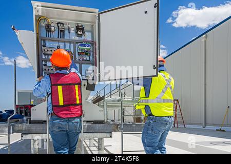 Zwei Bauarbeiter überprüfen die Schalttafel eines adiabatischen Kondensators auf dem Dach eines CO2-Kühllagers (Industriekühlung) Stockfoto