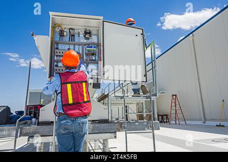 Zwei Bauarbeiter überprüfen die Schalttafel eines adiabatischen Kondensators auf dem Dach eines CO2-Kühllagers (Industriekühlung) Stockfoto