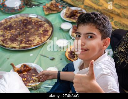 Porträt eines Jungen, der mit der Hand Vektorgeste oder zwei Zahlen macht, während er mit der Familie isst und lächelt Stockfoto