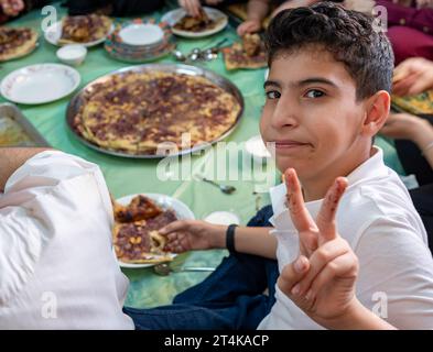 Porträt eines Jungen, der mit der Hand Vektorgeste oder zwei Zahlen macht, während er mit der Familie isst und lächelt Stockfoto