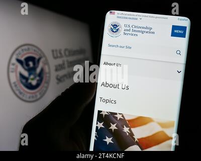 Person mit Smartphone und Website der US-Behörde Citizenship and Immigration Services (USCIS) mit Siegel. Konzentrieren Sie sich auf die Mitte des Telefondisplays. Stockfoto