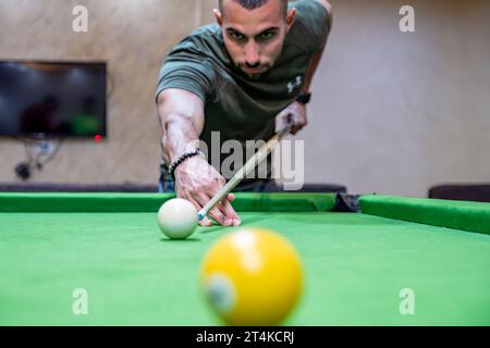 Junger Erwachsener bärenmännchen, der mit seinen Freunden Billard spielt und sich auf weißen Ball konzentriert, um ihn mit muskulöser Hand zu schlagen Stockfoto