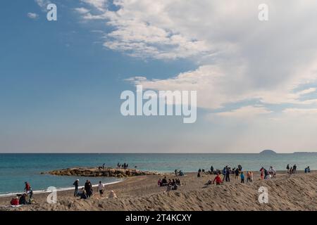 Menschen am Strand des beliebten Urlaubsziels, mit der Gallinara Insel am Horizont im Frühling, Loano, Savona, Ligurien, Italien Stockfoto