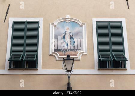 Votivschrein mit einem Fresko der Jungfrau Maria zwischen zwei geschlossenen Fenstern im historischen Zentrum von Loano, Savona, Ligurien, Italien Stockfoto