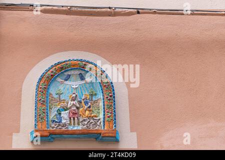 Votivschrein aus polychromer Keramik, der die Taufe Jesu durch Johannes den Täufer an der Fassade eines Hauses in Loano, Savona, Ligurien, Italien darstellt Stockfoto