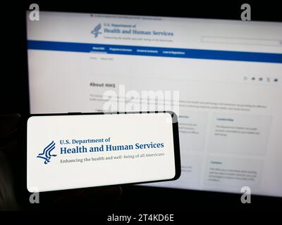 Person mit Smartphone und Logo des US-Gesundheitsministeriums (HHS) vor der Website. Schwerpunkt auf dem Display des Telefons. Stockfoto
