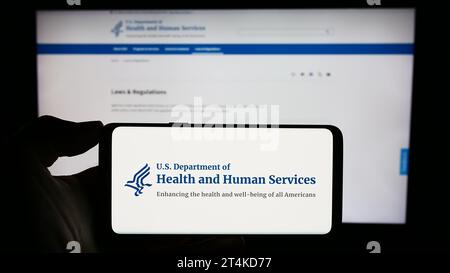 Person, die ein Mobiltelefon mit dem Logo des US Department of Health and Human Services (HHS) vor der Webseite hält. Schwerpunkt auf dem Display des Telefons. Stockfoto