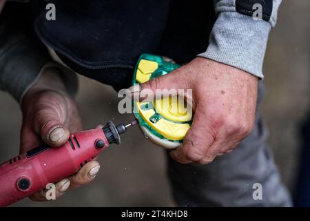 Man Farrier, der Kunststoff-Hufeisen am Hufhufeisen installiert. Detailansicht der Hände, die Tierfüße halten, und des Drehwerkzeugschleifers. Stockfoto