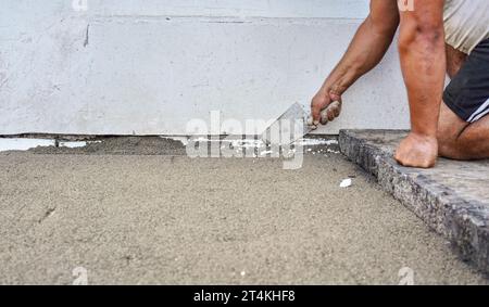 Installation von neuem Pflaster oder Boden außerhalb von großen Betonziegeln, Nahaufnahme des männlichen Arbeiters, der Sand- und Kies-Grundschicht in der Nähe der Wand befestigt. Stockfoto