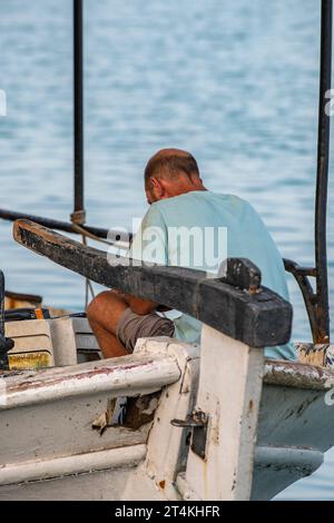 altgriechischer Fischer, der auf einem traditionellen Fischerboot im ionischen Hafen von zakynthos oder in der Stadt zante in griechenland sitzt, Stockfoto